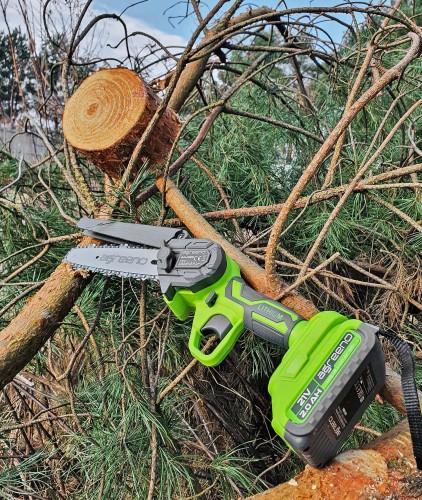 Akumulatorowa pilarka łańcuchowa marki Agreeno leżącą na ściętej gałęzi drzewa iglastego.