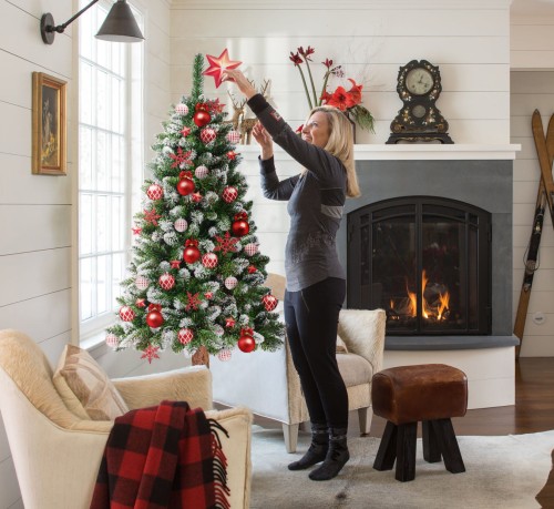 Choinka udekorowana świątecznymi ozdobami w kolorach czerwonym i białym na tle salonu z kominkiem.