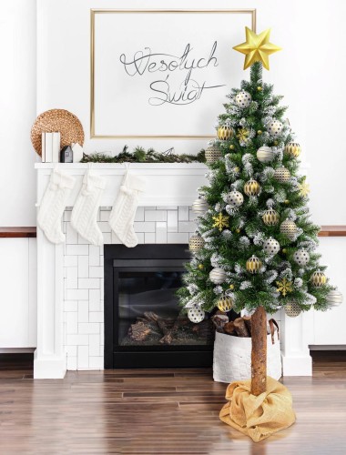 Choinka udekorowana świątecznymi ozdobami w kolorach srebrnym i złotym na tle salonu z kominkiem.