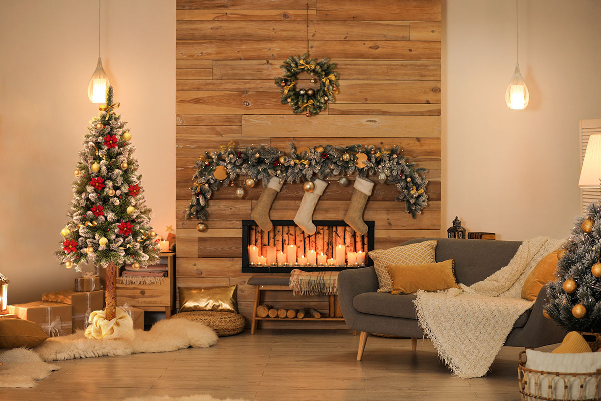 Choinka udekorowana świątecznymi ozdobami w kolorach czerwonym i złotym na tle salonu z kominkiem.
